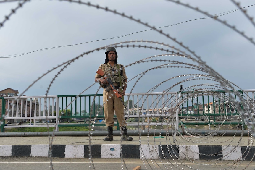 Security guard holds a gun and stands in front of wire fence