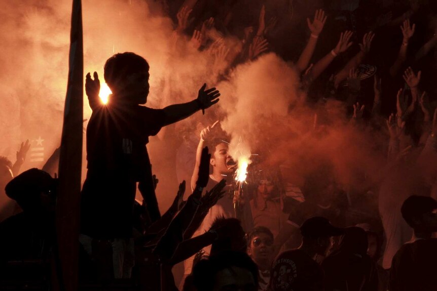 A football fan holds his arms out as others light flares.