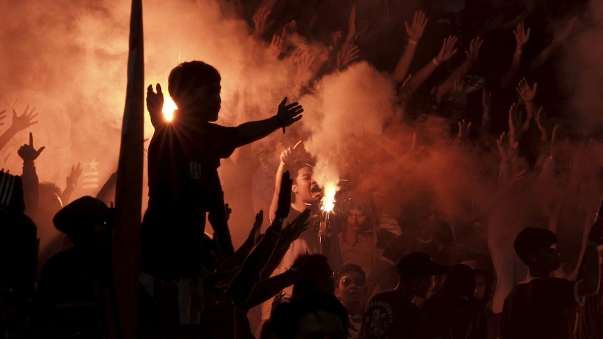 A football fan holds his arms out as others light flares.