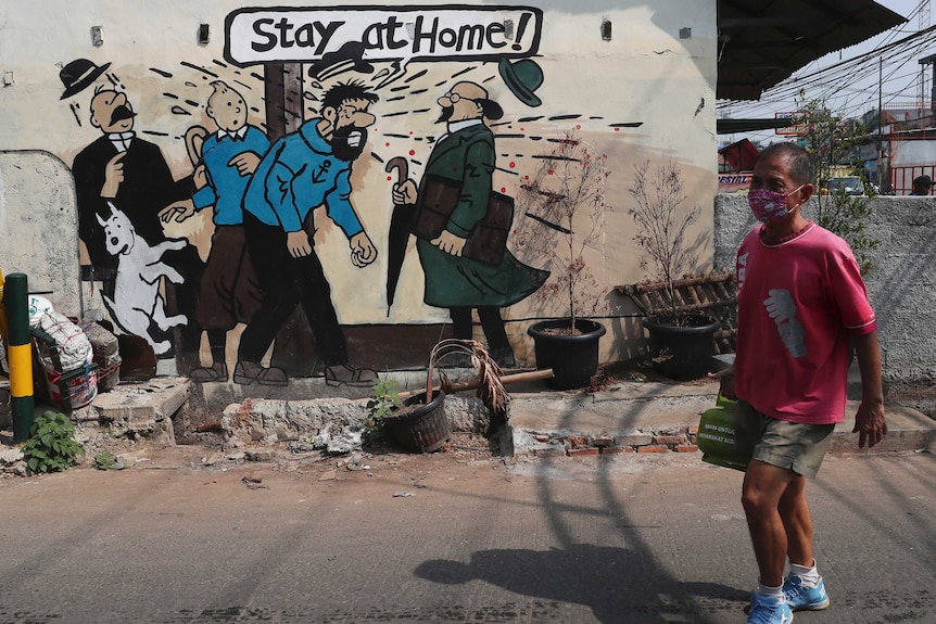 A man walks past a mural reading "stay at home!" with characters from the comic Tintin.