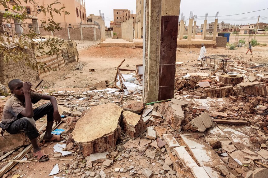An African youth sits on edge of destroyed house in dusty suburban area