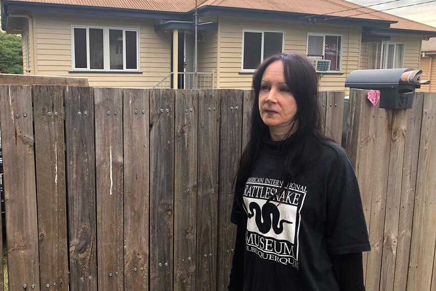 A woman standing at the front fence of a weatherboard house