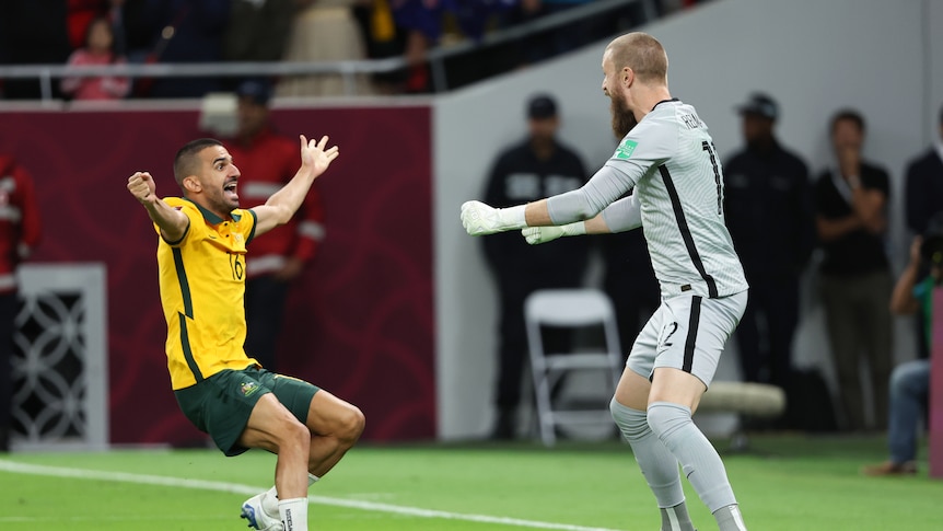 Two male soccer players, one wearing yellow and green and the other wearing grey, celebrate