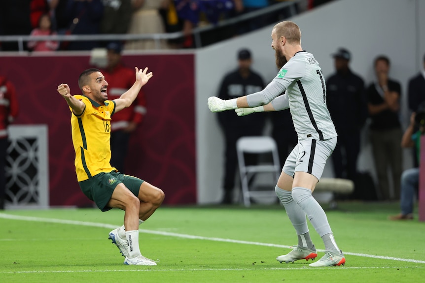 Two male soccer players, one wearing yellow and green and the other wearing grey, celebrate
