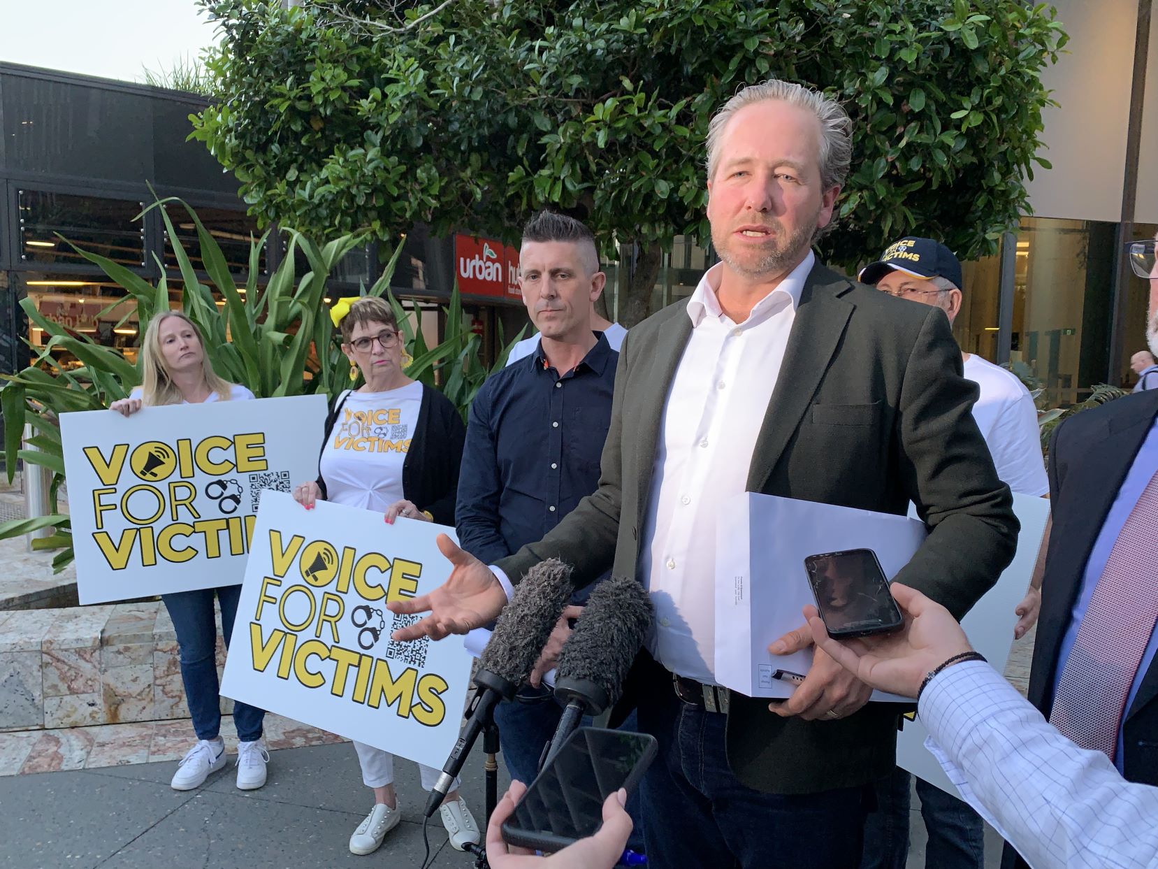 People speaking to media and holding Voice for Victims signs.