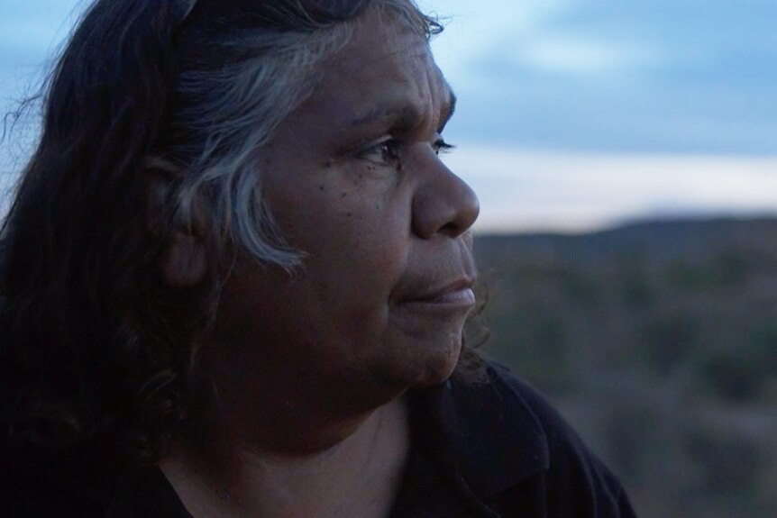 An older Aboriginal woman, Carol Turner, looking out on the desert landscape in In My Blood It Runs