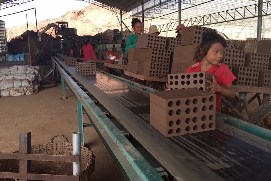 A girl unloading bricks from conveyor belts in Cambodia