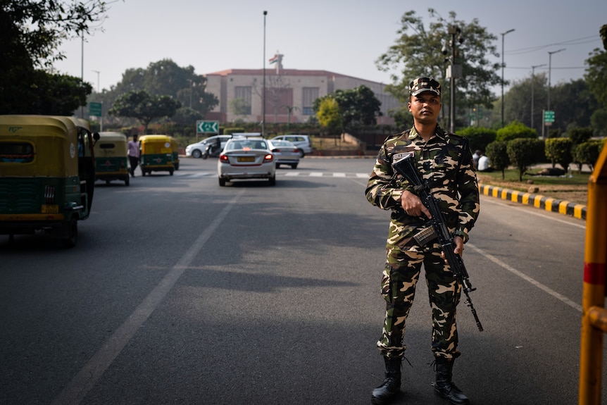 An Indian paramilitary soldier stands guard at a checkpoint holding a gun.