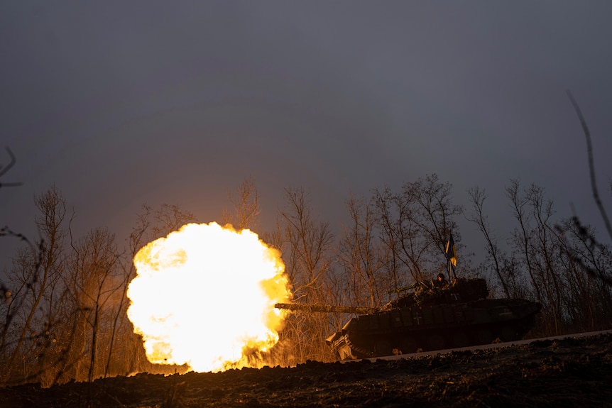 an explosion can be seen as a tank fires in front of trees in Ukraine