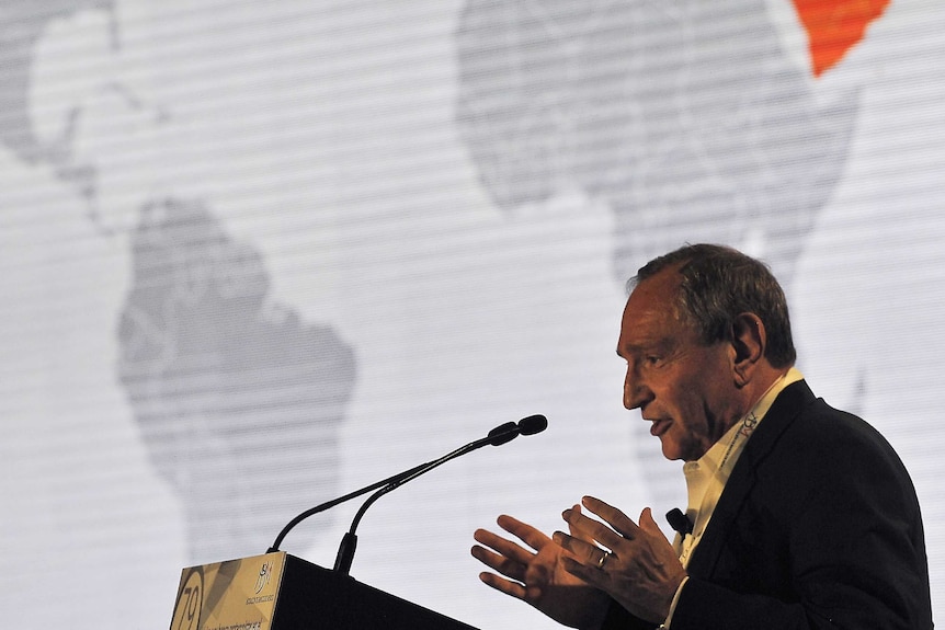 Geopolitical analyst George Friedman speaks from a podium with a world map in the background.