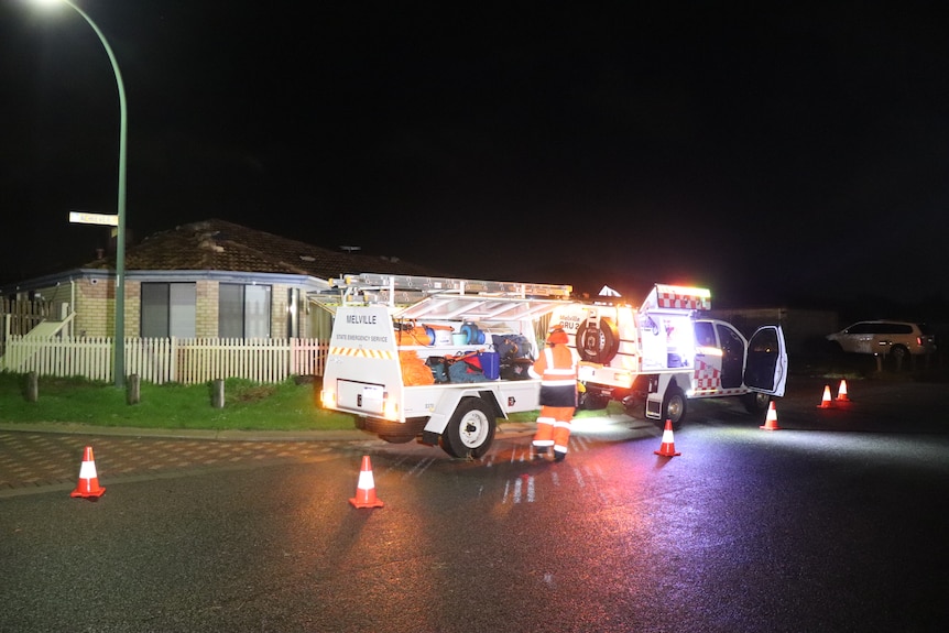 A wide shot of an emergency services vehicle outside a home damaged by bad weather at night.