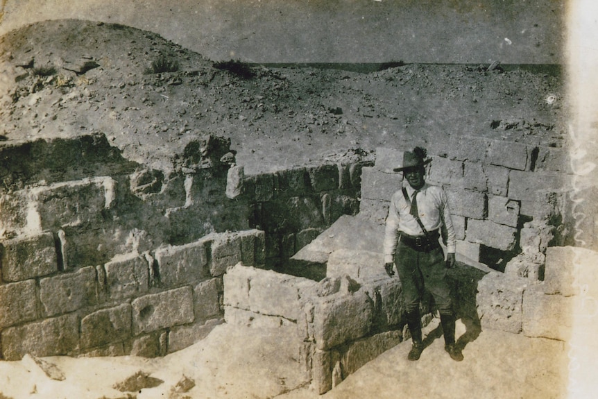 A black and white photo of a man standing among ruins in the desert