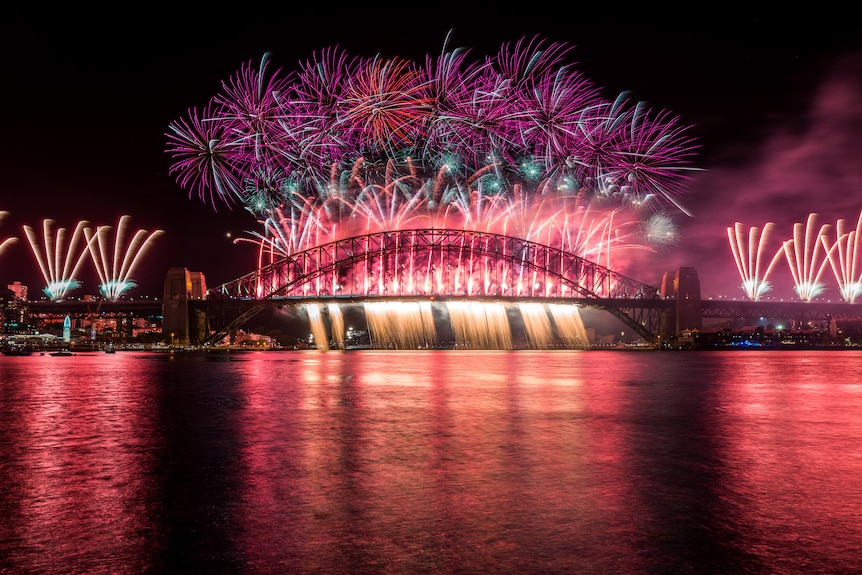 Colourful fireworks over the Sydney Harbour Bridge are reflected on the water below.