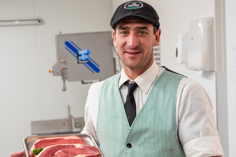 A butcher holds a tray of meat.