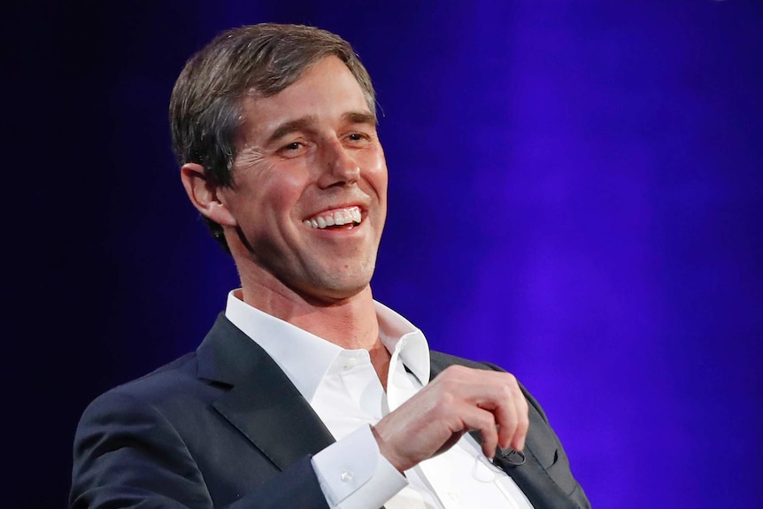Beto O'Rourke smiles while seated in a chair.