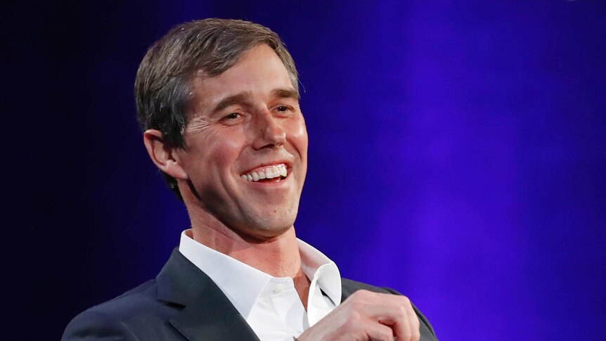 Beto O'Rourke smiles while seated in a chair.