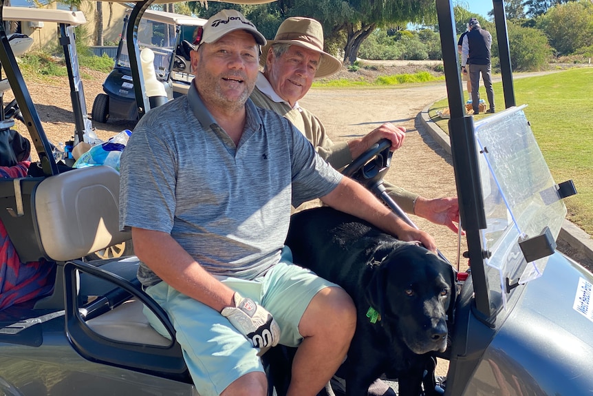 Two men and a dog in a golf buggy.