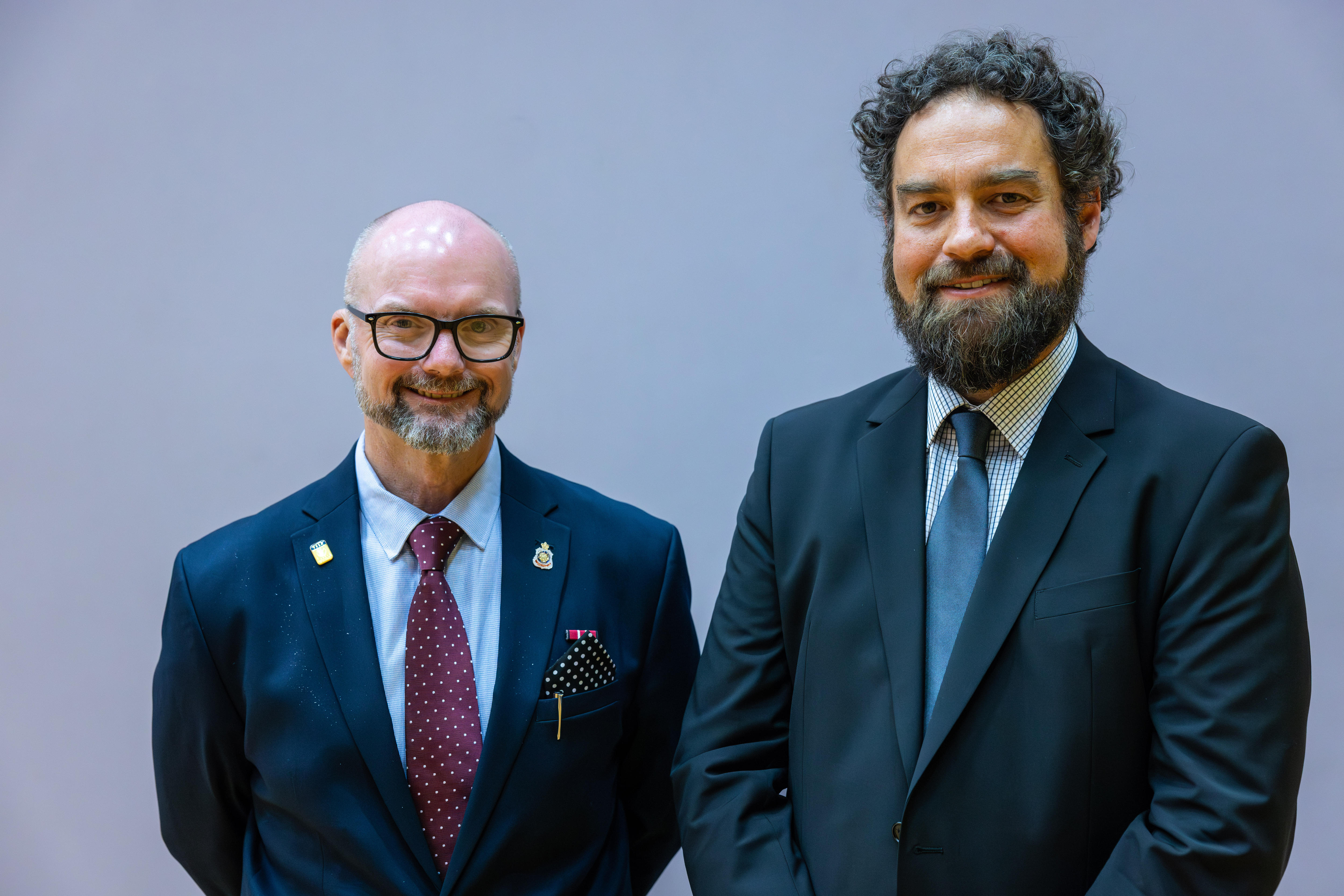 Dois homens de terno e gravata juntos contra um fundo simples