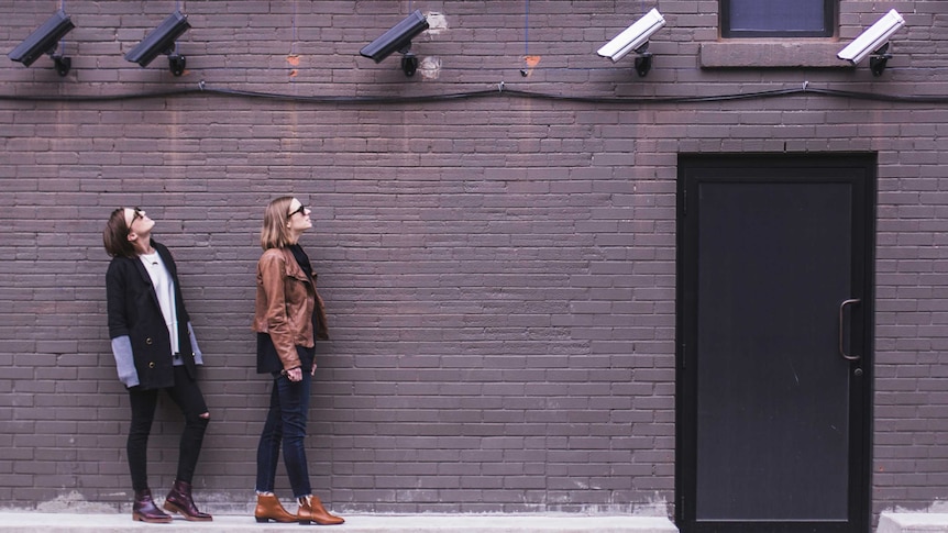 Two women look up at multiple CCTV cameras