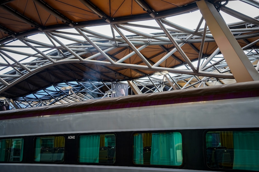 Criss-crossing and undulating roof of Southern Cross Station, with a train underneath producing what appears to be fumes.