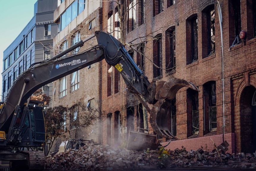 Large machinery is used to clear rubble below the burned building.