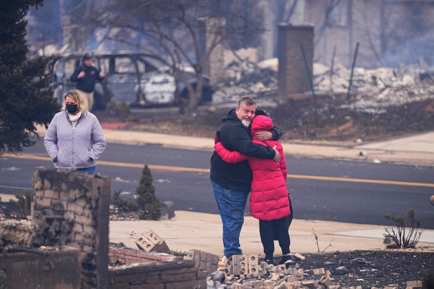 A man hugs a woman as they stand amid the ruins of a burned out house.