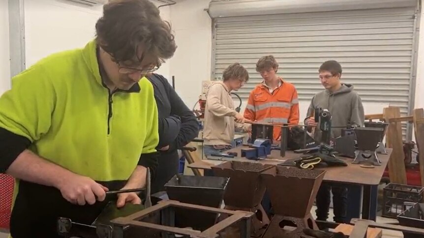 Older high school students on the tools in a metalwork shop.