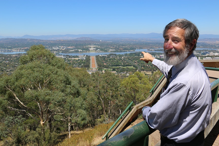Eric Martin stands at Mount Ainslie Lookout pointing down at Anzac Parade.