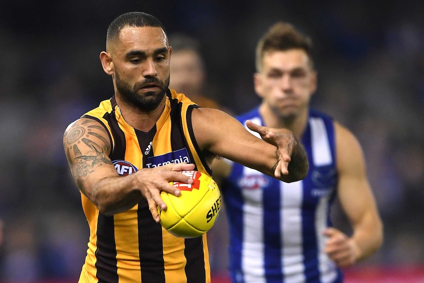 A Hawthorn AFL player holds the ball with his right hand as he prepares to kick it against North Melbourne.