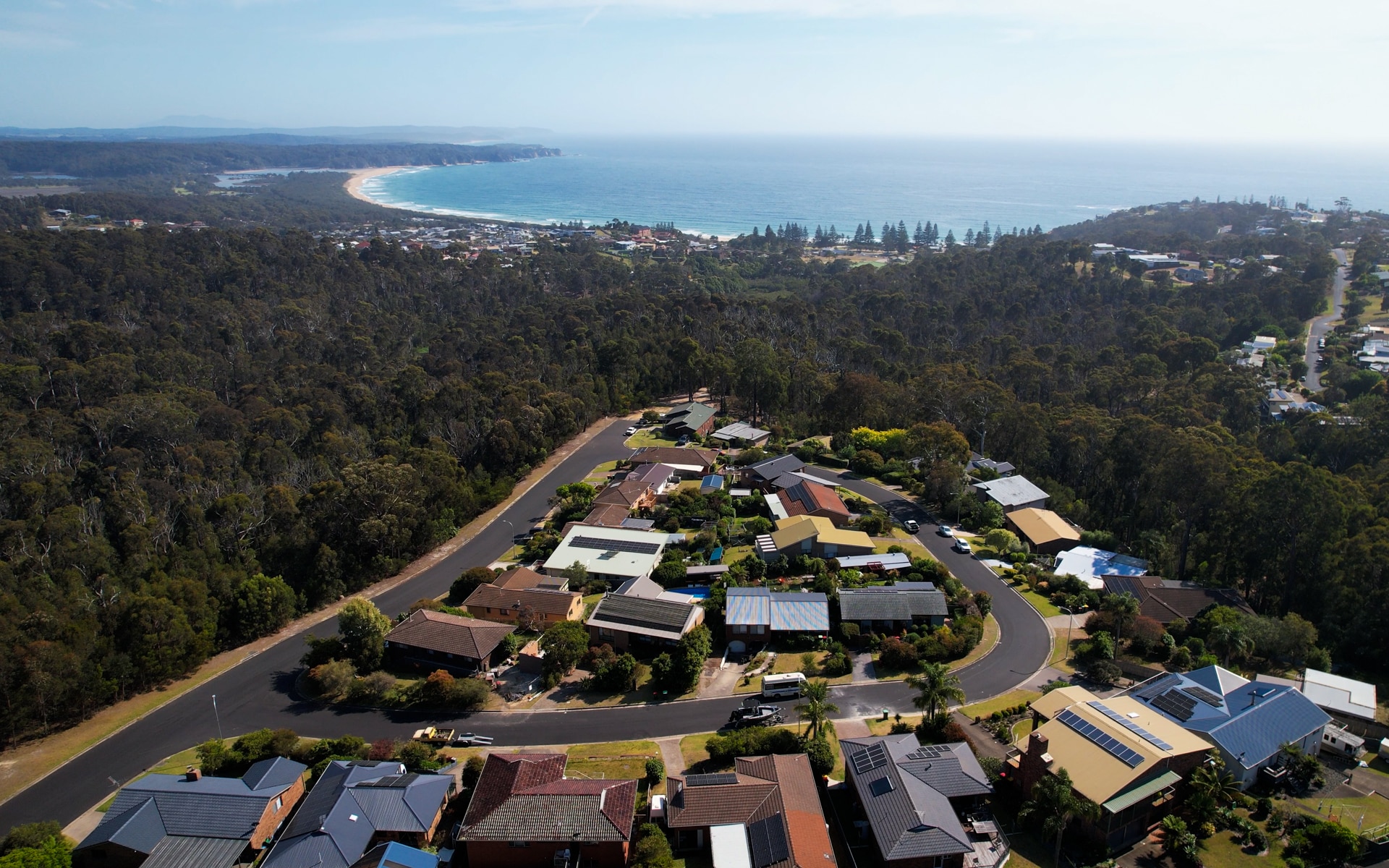 Vista aérea de una calle suburbana rodeada de bosque y una playa a lo lejos