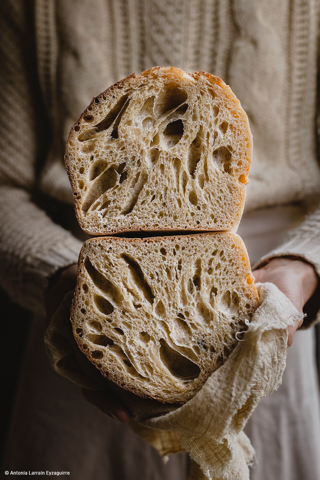 Two halves of a freshly-baked sourdough are held on top of each other to reveal the cross section. 