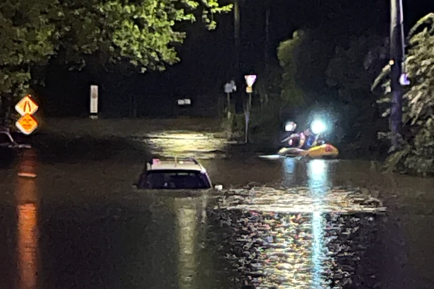 A rescue crew in a rubber boat paddle out in flood water to a car surrounded by water.