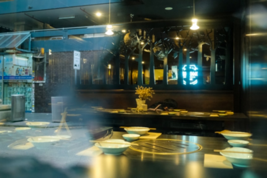 The view through the window of an restaurant, with bowls and chopsticks on the tables.