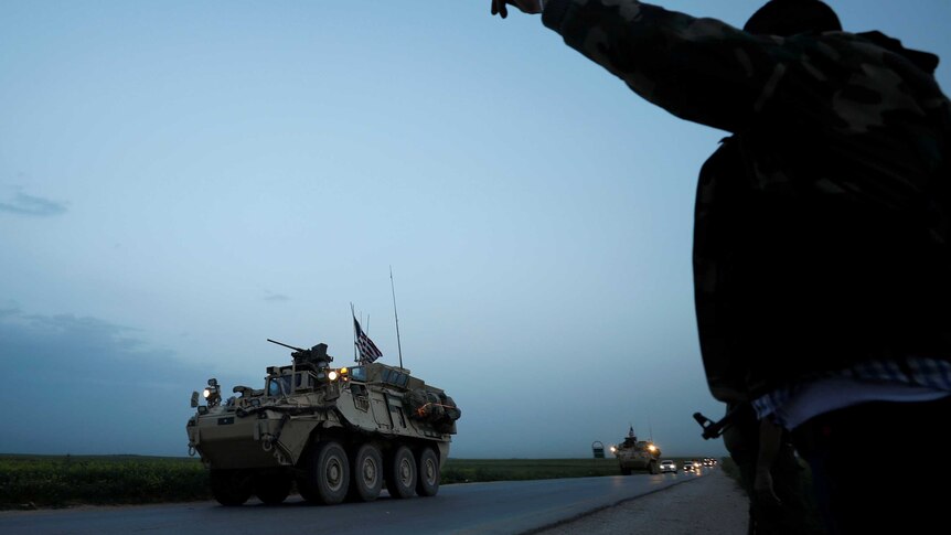 A Kurdish YPG fighter gestures at a convoy of US military vehicles.