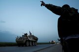 A Kurdish YPG fighter gestures at a convoy of US military vehicles.