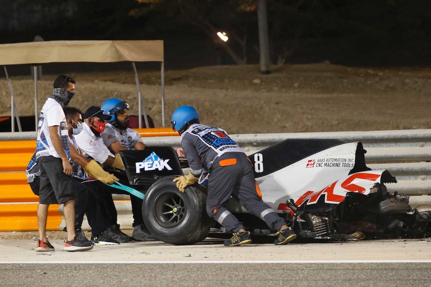 Stewards attempt to clear the car of Haas' Romain Grosjean from the track following a crash