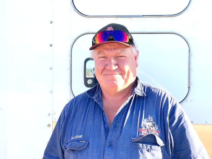 A close up photo of a male truck driver standing against a truck. He's smiling.
