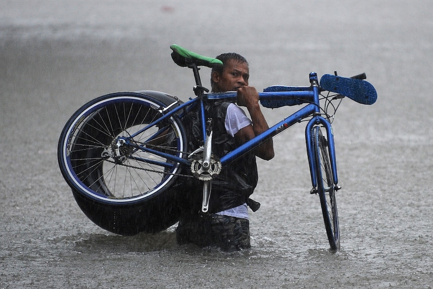 A man carries his bicycle through flooded Manila