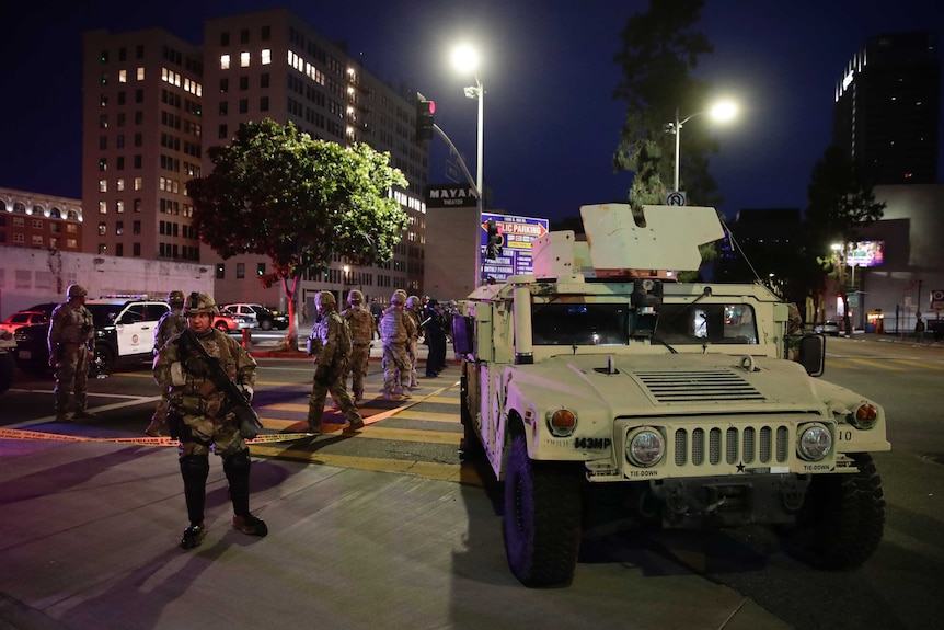 Armed soldiers stand on a blocked off street near an armoured Humvee