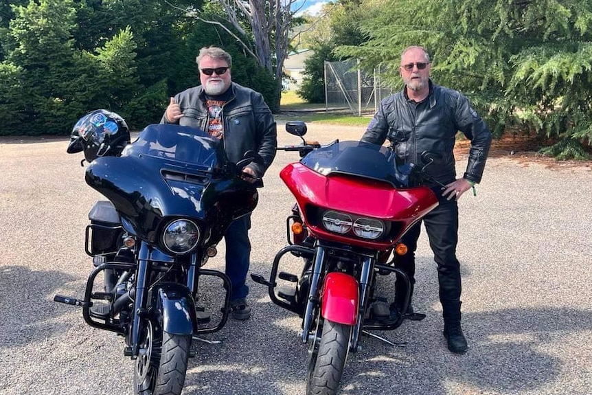 Two bikers standing next to their motorcycles.