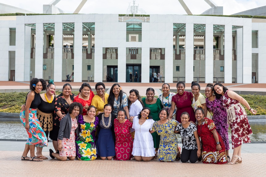 A group of 21 women standing outside parliament house, arms around each other. 