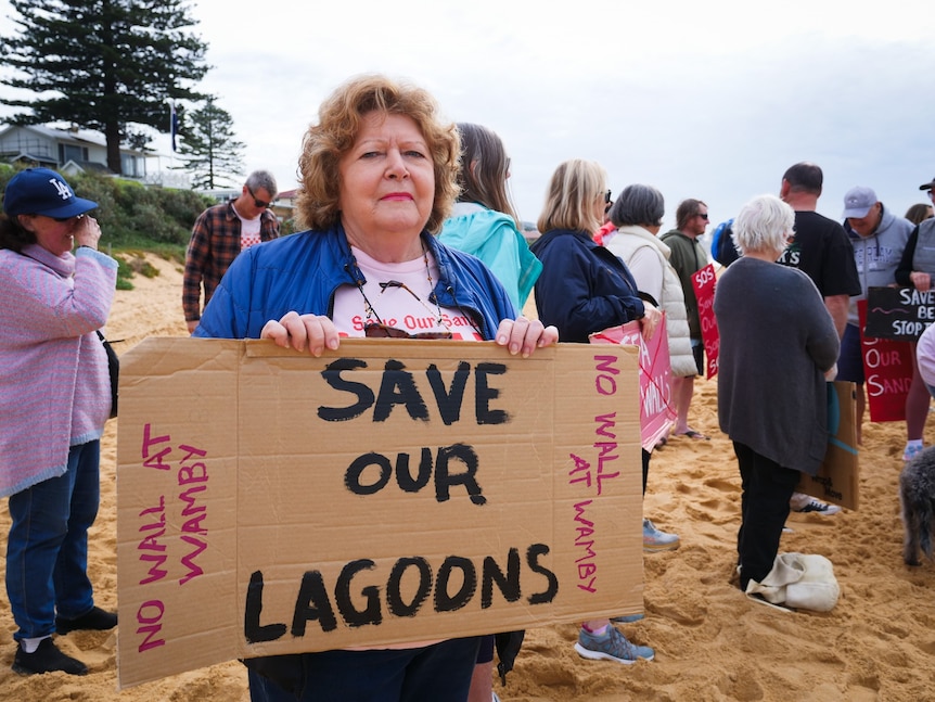 Eleanor Harrison holding a 'save our lagoons' sign at Wamberal Beach.