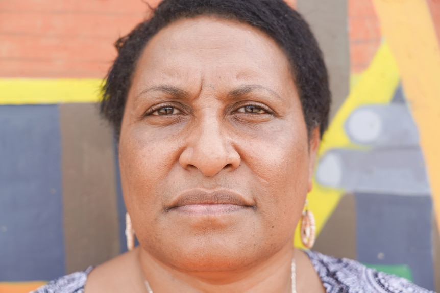 A woman with dark hear and wearing earings stares at the camera.