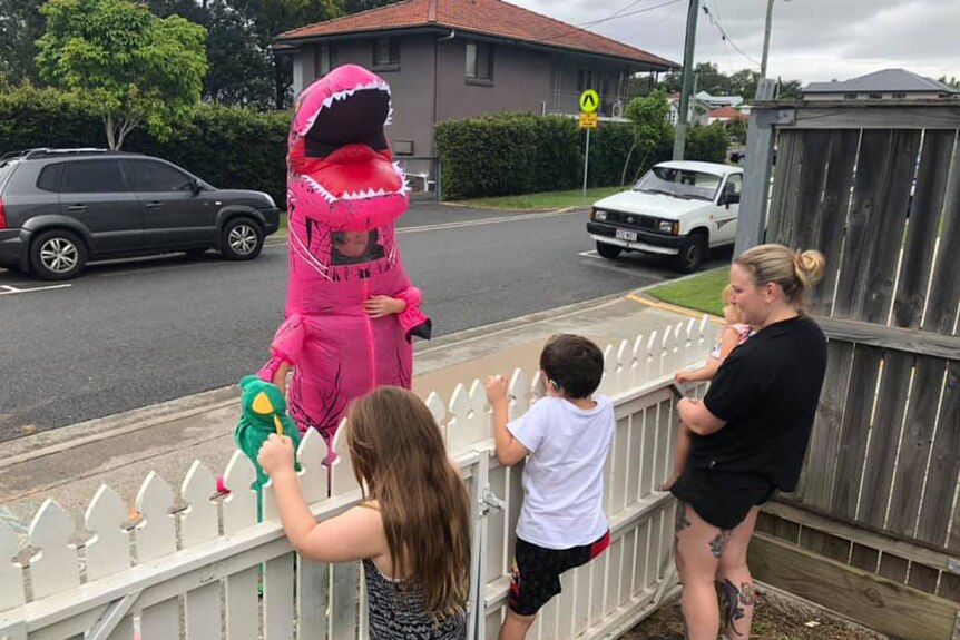 Brisbane resident Lucy Mangan, with her three children, meets Lou the dinosaur over the fence.