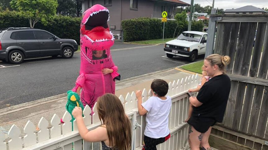 Brisbane resident Lucy Mangan, with her three children, meets Lou the dinosaur over the fence.