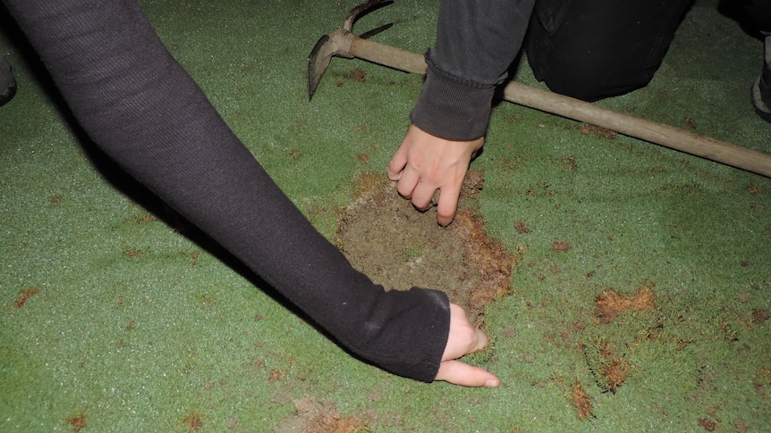 Two hands are seen filling a golf course hole with cement.