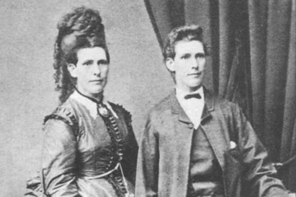 Old fashioned black and white photo of person with long hair and dress next to identical person in suit jacket and pants.