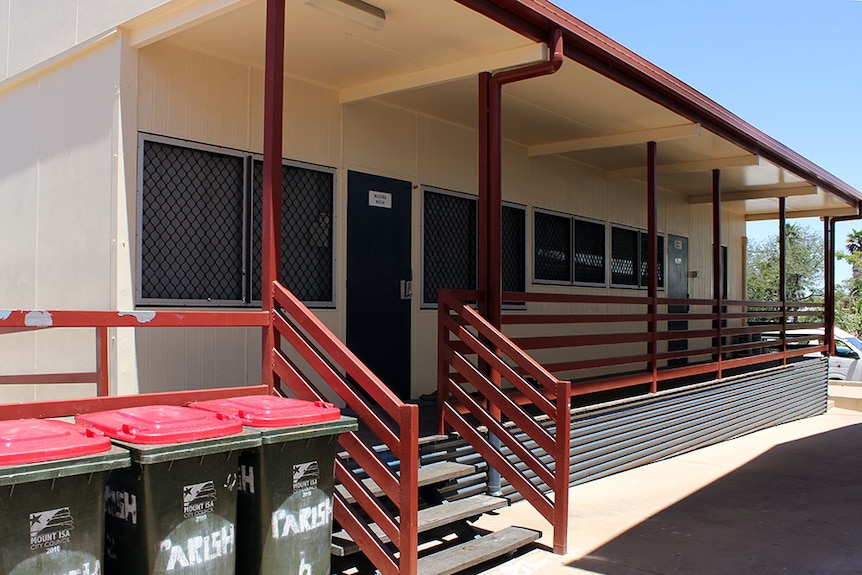 A cream-coloured demountable building with timber steps, railings and decking.