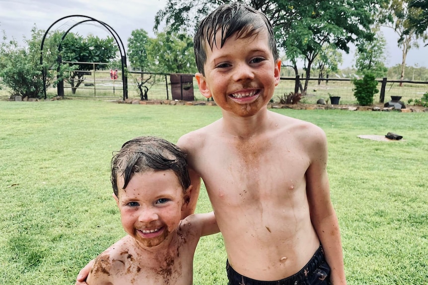 Two young kids grinning at the camera, covered in mud.