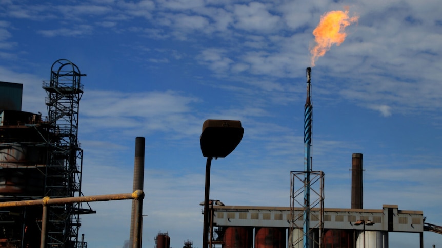 A steelworks site with gas pipe flame flare, sky with scattering of clouds, dusk.